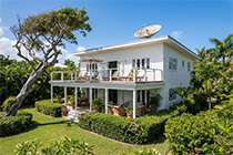 Ferienhaus Sonnendeck in Waldkiki - Zweistöckiges weißes Ferienhaus mit Radar auf dem Dach, umgeben von einem grünem Garten